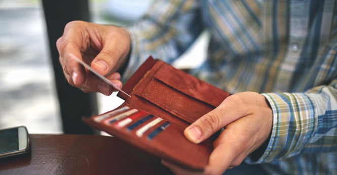 Right hand putting in a MedicAlert wallet card in a brown wallet being held by the left hand.