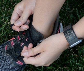 Woman tying her shoe laces while wearing a black apple watch with a black medical ID