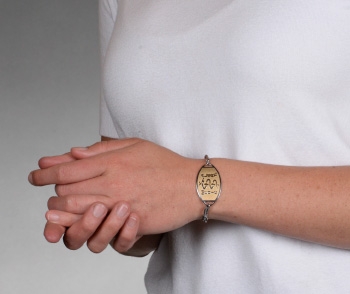 A person wearing a two tone classic large embossed silver medical ID bracelet with gold oval MedicAlert emblem and logo