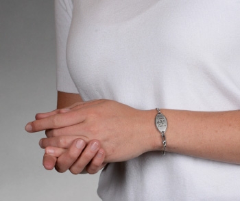 A person wearing a stainless steel petite embossed medical ID bracelet with oval MedicAlert emblem