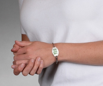 Person wearing classic medical ID bracelet in stainless steel with green MedicAlert logo on front of oval emblem 