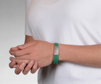 Person wearing a green silicone medical ID bracelet with rectangle MedicAlert emblem