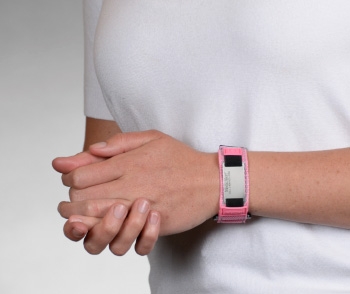A person wearing a pink reflective medical ID bracelet with fabric band, square rectangle MedicAlert emblem and logo