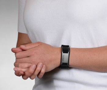 A person wearing a black reflective medical ID bracelet with fabric band, square rectangle MedicAlert emblem and logo