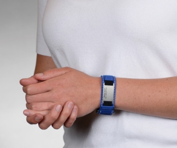 A person wearing a blue reflective medical ID bracelet with fabric band, silver rectangle MedicAlert emblem and logo